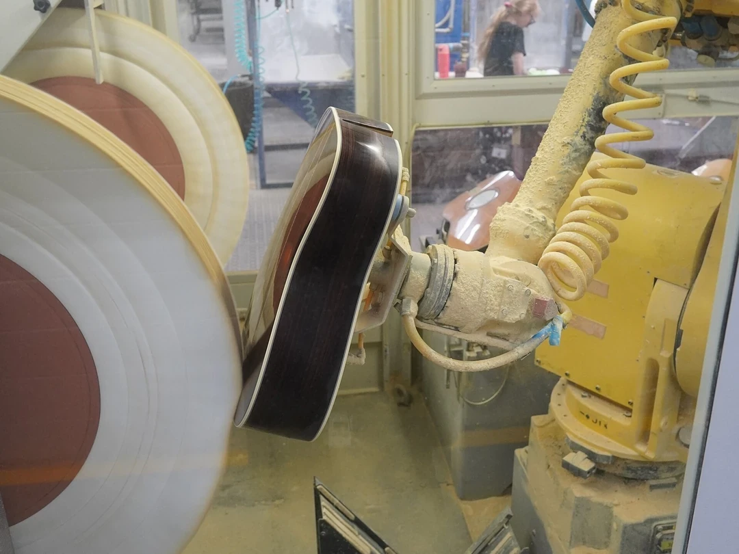 工場でギターのボディを磨く際に吸引ツールを使う産業用ロボットアーム