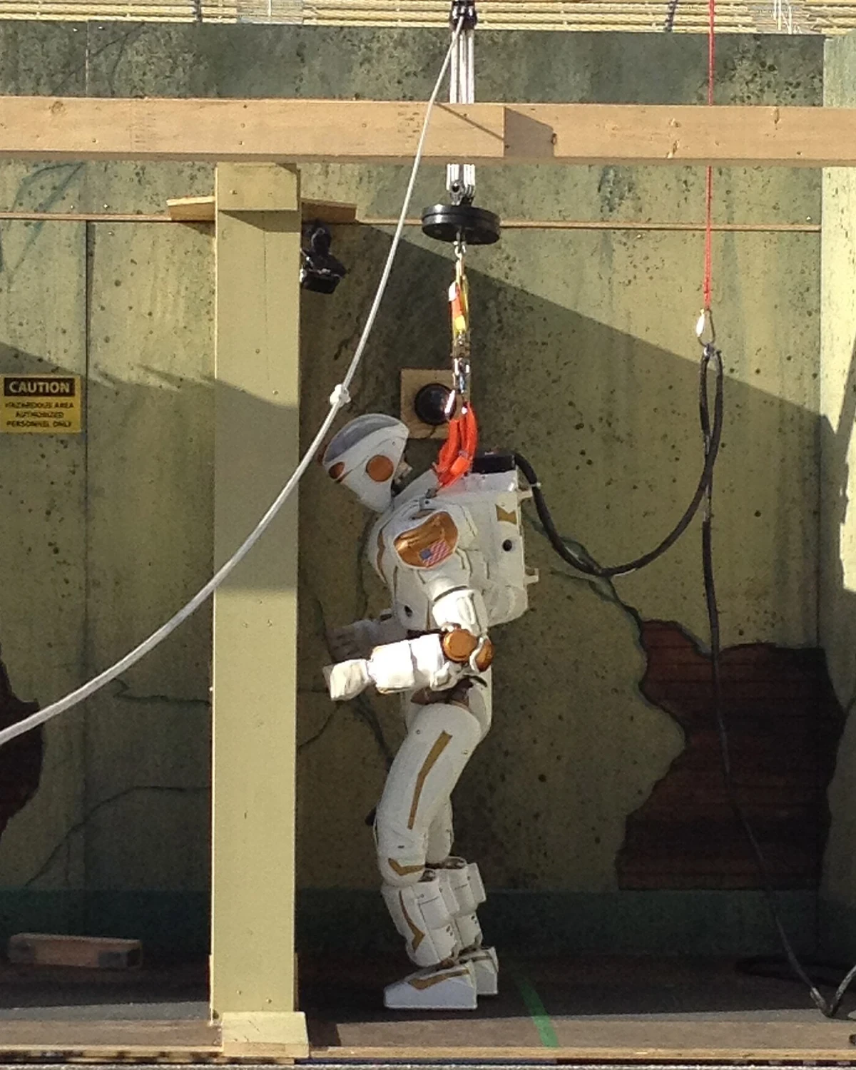 NASA Valkyrie humanoid testing a door handle while connected to a safety rig