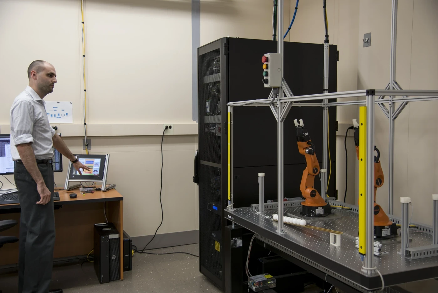Engineer beside connected industrial robots computing equipment and safety fencing in a manufacturing testbed